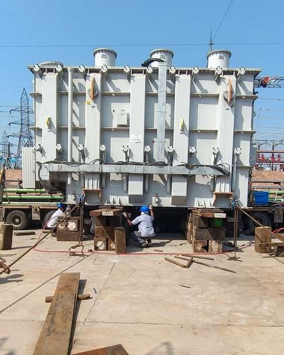 Transformer being jacked off a trailer onto stacks of timber sleepers by a rigging crew.