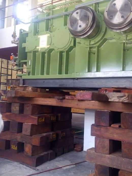 Heavy gearbox resting on stacked timber cribbing inside a plant.