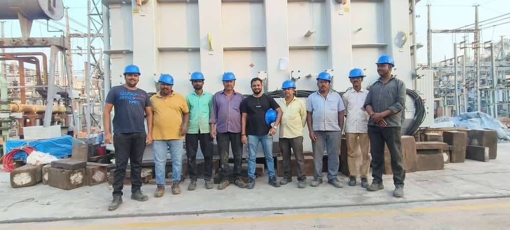 The Laxmi Enterprises rigging crew standing together in front of a power transformer at a substation.